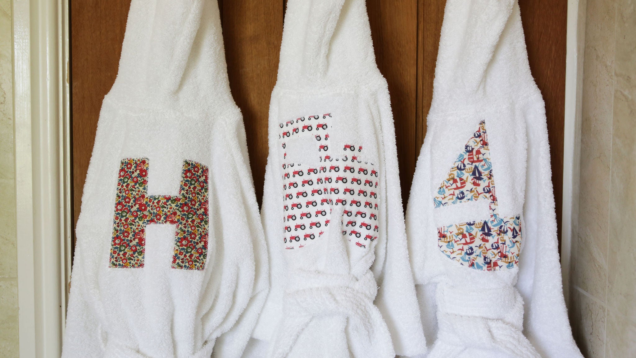3 chidren's hooded robes with a letter H, Tractor and Boat appliqued on to the back in a variety of colourful Liberty prints